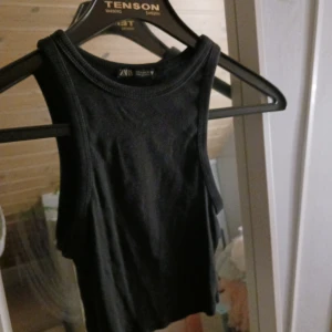 Svart ribbad linnetopp från Zara - Snygg svart ribbad linnetopp från Zara. Perfekt för en stilren look med sin ärmlösa design och bekväma passform. Passar utmärkt till både jeans och kjol.