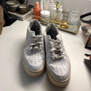 Vita Nike Air Force sneakers - Säljer ett par klassiska vita Nike Air Force sneakers. Skorna har en stilren design med snörning och perforerade detaljer för ventilation. Perfekta för en avslappnad stil.