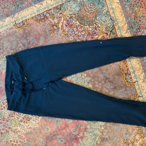 Mörkblå mjukisbyxor med snörning - Snygga mörkblå mjukisbyxor med snörning i midjan. Perfekta för en avslappnad stil. Byxorna har en bakficka och är tillverkade i ett mjukt material för extra komfort.