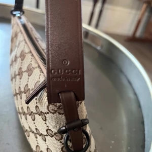 GUCCI GG Canvas Mini Pochette Pouch Bag - Snygg GUCCI GG Canvas Mini Pochette Pouch Bag i beige och brunt med det klassiska GG-mönstret. Väskan har en dragkedja upptill och en  axelrem i brunt läder. Perfekt för att bära dina nödvändigheter med stil. Väskan kommer med original kartong och tygpåse.