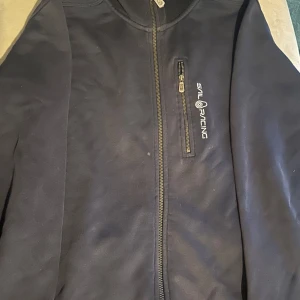 Marinblå jacka från Sail Racing - Snygg marinblå zip up hood från Sail Racing med dragkedja och logotyp på bröstet. Hoodien har långa ärmar och en praktisk bröstficka med dragkedja. Perfekt för en sportig look.