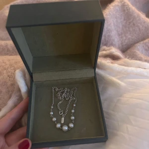 Halsband med pärlor från Maria Nilsdotter - Box medföljer, modellen Dawn necklace nypris runt 3000(?), använt fåtal gånger! Elegant halsband från Maria Nilsdotter med en kedja i silver och vackra vita pärlor. Perfekt för att ge en stilren touch till din outfit. Fint skick, dock kan man kanske se spår av användning på silverbrickan vid låset! (Men inget som syns på halsbandet i sig)