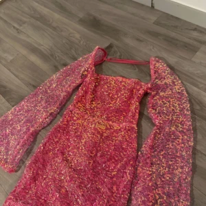 Rosa glittrig klänning - Säljer en fantastisk rosa klänning med glittriga paljetter och långa ärmar. Klänningen har en tight passform och en öppen rygg som ger en elegant touch. Perfekt för en festlig kväll!