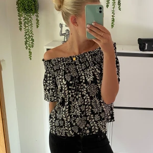 Svart och vit offshoulder topp från H&M - Säljer en snygg offshoulder topp från H&M i svart och vitt med blommigt mönster. Toppen har korta ärmar och en elastisk kant upptill för en bekväm passform. Använd fåtal gånger därmed inga defekter❣️💞