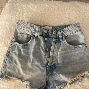 Jeansshorts från Zara - Snygga ljusblå jeansshorts från Zara med fransiga kanter och knappgylf. Har tecken på användning men inga defekter. Köpta förra året 