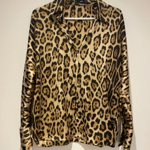 Leopardmönstrad skjorta från MNG - Snygg leopardmönstrad skjorta från MNG i ett glansigt material. Skjortan har långa ärmar och knappar framtill. Perfekt för att ge din outfit en djärv touch 🐆