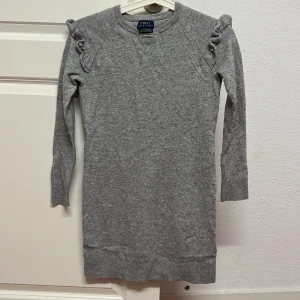 Grå klänning från Polo Ralph Lauren - Snygg grå klänning från Polo Ralph Lauren med volangdetaljer vid axlarna. Klänningen är långärmad och har en bekväm passform, perfekt för kyligare dagar. Knappt använd 