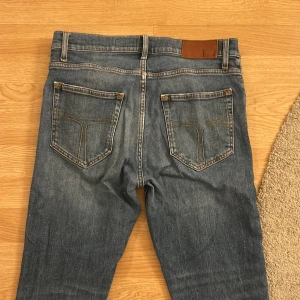 Blå jeans från Tiger of Sweden - Säljer ett par klassiska blå jeans från Tiger of Sweden i modellen Pistolero. De har en snygg straight passform och är tillverkade i slitstarkt denim. Perfekta för en stilren look.