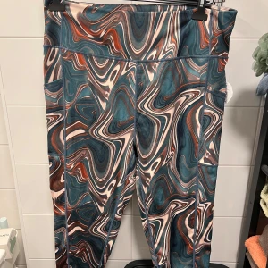 Mönstrade leggings från XLNT - Snygga leggings med ett unikt, abstrakt mönster i blå, brun och beige. Perfekta för att ge din outfit en färgglad touch. De är stretchiga och bekväma, vilket gör dem idealiska för både avslappnade dagar och mer aktiva stunder.