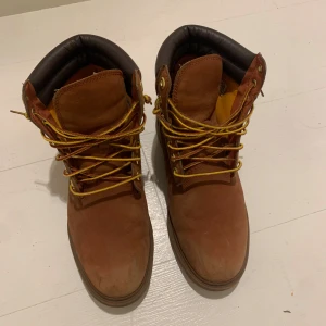 Bruna boots från Timberland - Säljer ett par klassiska bruna Timberland boots med snörning och vadderad krage. Perfekta för höst och vinter med robust design och slitstarkt skinnmaterial. Använda en säsong. 
