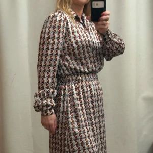 Mönstrad klänning från Orsay - Snygg mönstrad klänning från Orsay i en mix av blått, vitt och rött. Klänningen har långa ärmar med knappar vid ärmsluten och en bekväm passform. Perfekt för en stilfull look.