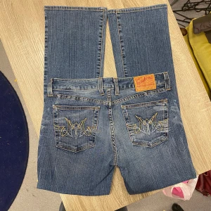 Lågmidjade Jeans Bootcut Flare - Snygga jeans med en bootcut passform i storlek 31. Ifrån märket Lucky Brand med snygga detaljer på bakfickorna. Mått finns bifogade nedan!  I bra skick med en fläck som syns på sista fotot  Mått Midja: 39cm Gren: 21cm Fotöppning: 23cm Innerbens längd: 78cm  Storlek 12/31  Kolla gärna igenom mina andra annonser! 