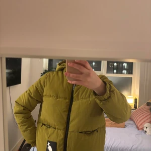 Grön pufferjacka från Kangol - Säljer en grön pufferjacka från Kangol med dragkedja och huva. Jackan har långa ärmar och en stilren design, perfekt för kyligare dagar. Den har en logotyp på framsidan och elastiska muddar vid ärmsluten. hm x Kangol. 