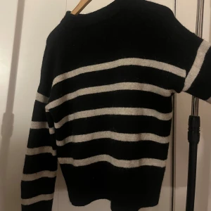 Svart och vit randig stickad tröja - Säljer en svart stickad tröja med vita ränder. Tröjan har långa ärmar och en klassisk rund hals. Perfekt för kyligare dagar. Storlek 38/40 men passar mig som har XS.