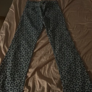 Mönstrade jeans med blommor 80/90 tal - Snygga jeans med ett unikt blommönster i blå och grå nyanser. Byxorna har en klassisk femficksdesign och stängs med dragkedja och knapp. Perfekta för dig som vill sticka ut med en cool stil.