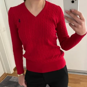 Röd kabelstickad tröja - Säljer en röd kabelstickad tröja som liknar Ralph Lauren. Den har en v-ringning och ett broderat märke på bröstet. Perfekt för både vardag och finare tillfällen nu i höst och vinter! Tröjan är i nyskick och inte använd!!❤️Pris kan såklart diskuteras!