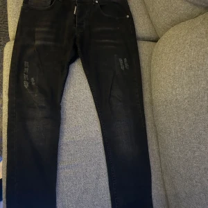 Svarta jeans från Dsquared2 - Snygga svarta jeans från Dsquared2 med slitna detaljer och klassisk femficksdesign. De har en dragkedja och knapp framtill samt en diskret logga vid fickan. Perfekta för en stilren look.