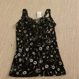 Svart blommig linnetopp - Säljer en svart linnetopp med blommigt mönster i vitt och grått. Köpt på second hand.