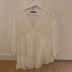 Vit klänning från Zara - Säljer en vit klänning från Zara med v-ringning och spetsdetaljer. Klänning har trekvartsärmar och en luftig passform, perfekt för vår och sommar. Tillverkad i ett lätt och bekvämt material. Är i L men är lite liten i storleken