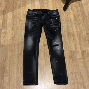 Svarta jeans med slitningar från Dondup - Snygga svarta jeans från Dondup med coola slitningar och färgstänk. De har en knappgylf och klassisk femficksdesign. Perfekta för en trendig look.