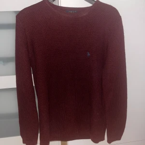Vinröd stickad tröja från Ralph Lauren - Säljer en snygg vinröd stickad tröja från Ralph Lauren med det klassiska logotypbroderiet på bröstet. Tröjan har en rund halsringning och långa ärmar, perfekt för kyligare dagar. Passar egentligen XL