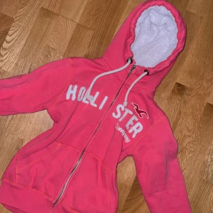 Rosa hoodie med teddyluva från Hollister - Säljer en mysig rosa hoodie från Hollister med vit teddyluva Perfekt för kyliga dagar!                                         Dragkedjan fungerar men har tappat själva grejen man håller i. Men en ovanlig modell i dessa koftor med Teddy materialet. Super cool!