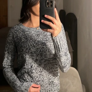 Gråmelerad stickad tröja - Säljer en supermysig gråmelerad stickad tröja. Den har en klassisk rund hals och långa ärmar, perfekt för kyliga dagar. Tröjan är i ett mjukt material som känns skönt mot huden. Passar både till vardags och lite mer avslappnade tillfällen.