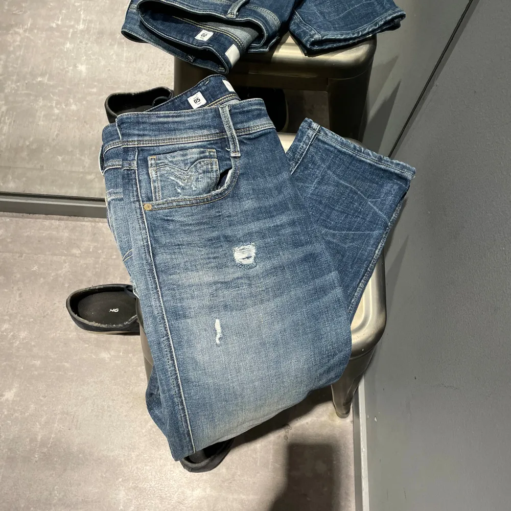 Säljer ett par snygga blå jeans från Replay i modellen Anbass. De har en slim fit passform och är tillverkade av hållbar bomull. Jeansen har en klassisk femficksdesign med slitna detaljer för en cool look. Perfekta för både vardag och fest!. Jeans & Byxor.