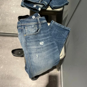 Blå jeans från Replay - Säljer ett par snygga blå jeans från Replay i modellen Anbass. De har en slim fit passform och är tillverkade av hållbar bomull. Jeansen har en klassisk femficksdesign med slitna detaljer för en cool look. Perfekta för både vardag och fest!