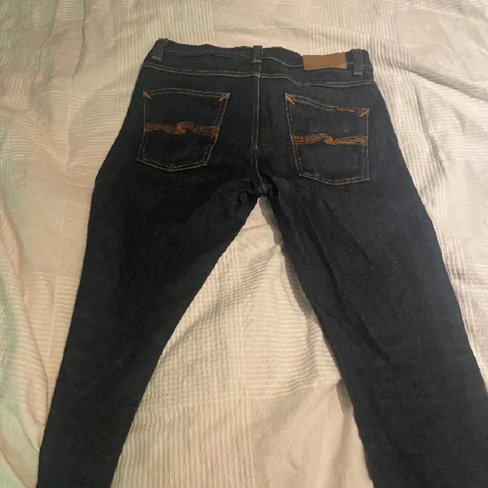 Säljer ett par snygga mörkblå jeans från Nudie Jeans. De har en klassisk design med orange sömmar och en bekväm passform. Perfekta för både vardag och fest! 31/34. Jeans & Byxor.