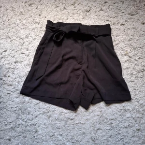 Svarta shorts från H&M - Säljer ett par snygga svarta shorts från H&M. De är högmidjade med ett knytband i midjan för en extra touch. Perfekta för både vardag och fest! Endast använda ett fåtal ggr.🖤 