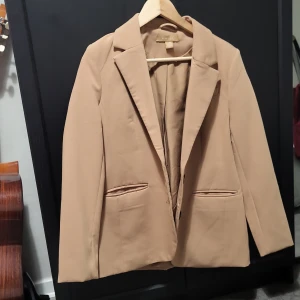 Beige kavaj från Amisu - Snygg beige kavaj från Amisu i klassisk design. Kavajen har långa ärmar och knappar vid ärmsluten. Perfekt för en stilren look.