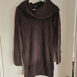 Brun stickad klänning från H&M - Mysig brun stickad klänning från H&M med en bred krage. Klänningen har långa ärmar och ribbade detaljer vid ärmslut och nederkant. Perfekt för kyliga dagar.