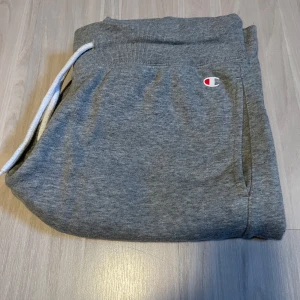 Grå shorts från Champion - Säljer ett par grå shorts från Champion med snörning i midjan och logotyp på benet. Perfekta för en avslappnad stil. De har en normal passform och är tillverkade i mjukt material för extra komfort.