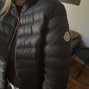 Svart dunjacka från Moncler - Säljer en snygg svart dunjacka från Moncler. Jackan har en dragkedja med röd och vit kant och ett Moncler-märke på ärmen. Har fler bilder, passar Xs/S, pris kan definitivt diskuteras, kan gå betydligt lägre i pris💗