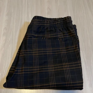 Rutig byxa med snörning - Snygga byxor med rutigt mönster i svart och brunt. De har en bekväm elastisk midja med snörning och raka ben. Perfekta för en avslappnad stil.