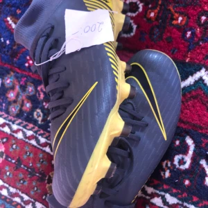 Grå fotbollsskor med gula detaljer - Snygga grå fotbollsskor med gula detaljer och snörning. Perfekta för fotbollsplanen med en stilren design och bra grepp.