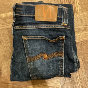 Mörkblå jeans från Nudie Jeans - Snygga mörkblå jeans från Nudie Jeans med orange sömmar och klassisk femficksdesign. Jeansen har en slim passform och är tillverkade i denim med en lätt tvättad look. Perfekta för en stilren vardagslook.