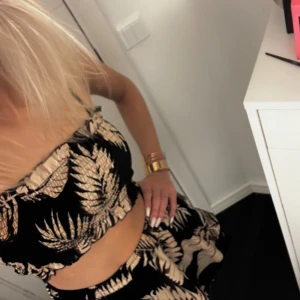 Svart och beige mönstrad klänning  - Säljer en snygg svart och beige klänning  med ett tropiskt mönster. Klänningen är ärmlös och har smala axelband. Perfekt för sommardagar och ger en trendig look.