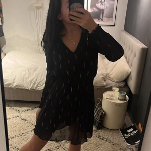 Svart klänning  - Säljer en svart klänning med färgglatt mönster och v-ringning. Klänningen har långa ärmar och en luftig passform som ger en bekväm känsla. Perfekt för att ge en färgklick till garderoben!