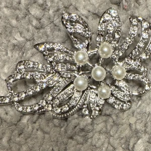 Glittrig brosch med pärlor - Elegant brosch i silverfärg med glittriga detaljer och vackra pärlor i mitten. Perfekt för att ge en extra touch av glamour till din outfit.