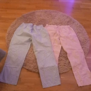 Randiga pjamas byxor i blått och rosa - Två par randiga pjamas byxor i gråblå och rosa färg. Använda väl, fläckar lite här och vad och det är därför jag säljer dom så billigt. De blå pjamas byxorna är ihop syda i skrevet. 1 par pjamas byxor för 10kr och 2 båda för 15kr💙🩷
