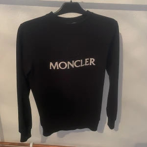 Svart tröja Moncler - Säljer en stilren svart tröja från Moncler med deras ikoniska logga broderad på framsidan. Tröjan har långa ärmar och en klassisk passform. Perfekt för en avslappnad och trendig look.