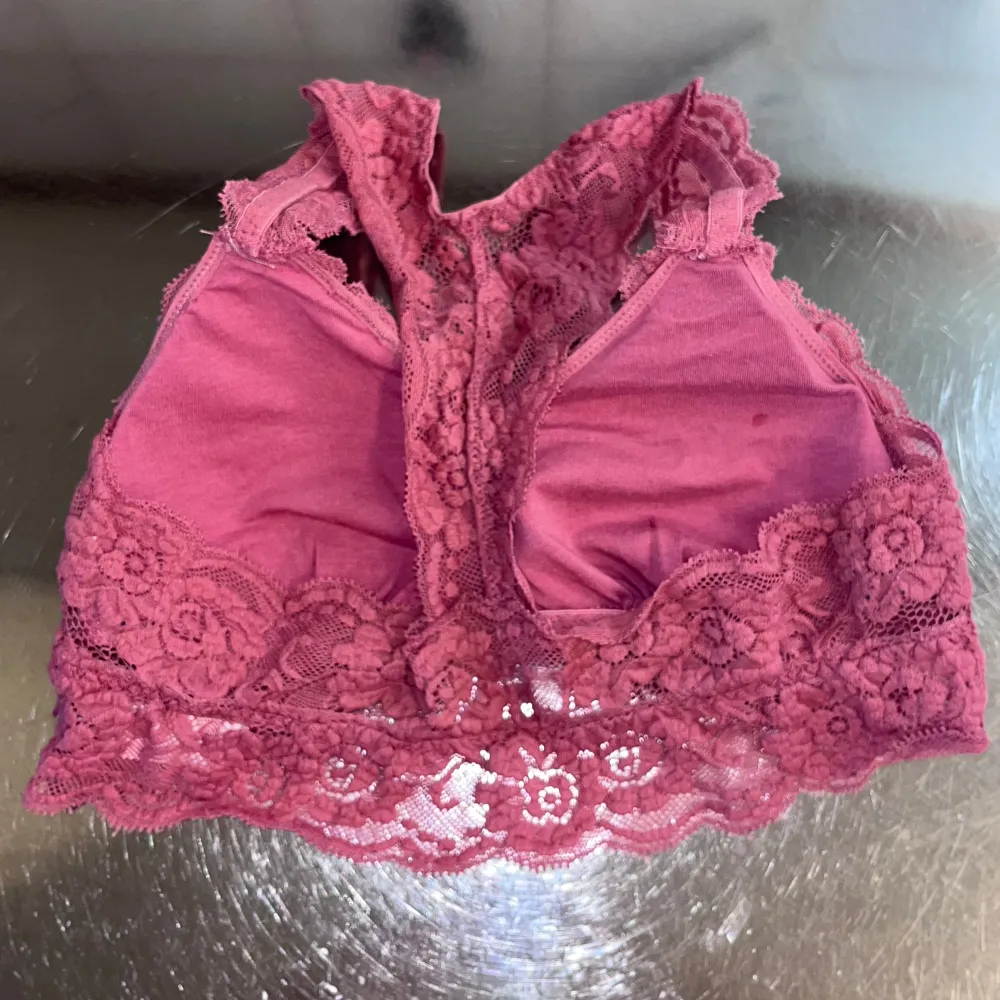 Säljer en söt rosa bralette i spets med blommigt mönster. Den har breda axelband och en vacker spetskant nedtill. Perfekt för att lägga till en romantisk touch till din outfit.. Muu.