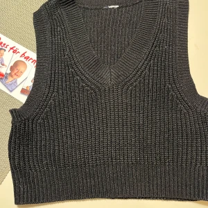 Svart stickad väst från H&M - Säljer en stilren svart stickad väst från H&M. Västen har en v-ringad design och är perfekt för lager-på-lager-stil. Den är ribbad vid kanterna vilket ger en snygg och modern look. Passar utmärkt över en skjorta eller t-shirt.