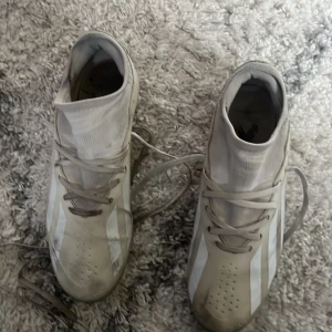 Beige fotbollsskor från Adidas - Säljer ett par beige fotbollsskor från Adidas med snörning och dobbar för bra grepp på planen. Skorna har de klassiska tre ränderna i vitt på sidan och är designade för optimal prestation.
