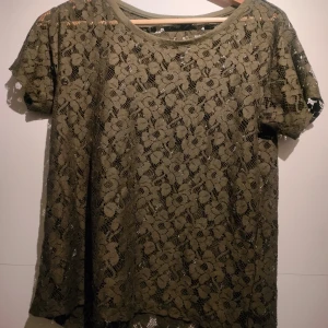 Olivgrön spetsblus från H&M - Säljer en olivgrön blus i spets från H&M i storlek XS. Blusen har korta ärmar och ett vackert blommigt mönster. Perfekt för att ge en romantisk touch till din outfit. 💚