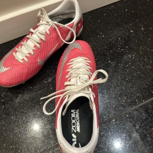 Nike Mercurial fotbollsskor - Snygga Nike Mercurial fotbollsskor i rosa och vit med snörning.  De är lätta och ger bra grepp på gräs. Använda max 2 gånger, dom säljes då dom inte passade mig! Ny pris 1400 såldes för 700! Pris går att diskutera 