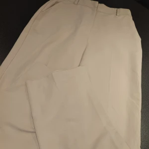 Beige kostymbyxor från NA-KD - Snygga beige kostymbyxor från NA-KD. Perfekta för en stilren look med en klassisk passform. Byxorna har en hög midja och är tillverkade i ett bekvämt material som ger en elegant känsla.