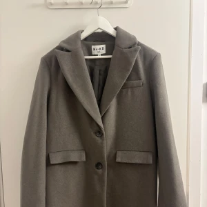 Kappa - Jättefin lång grå/beige kappa med två knappar köpt på NAKD för 1200 kr, men aldrig använd - så helt nytt skick! Den är i storlek 34, men passar absolut en 36a🫧